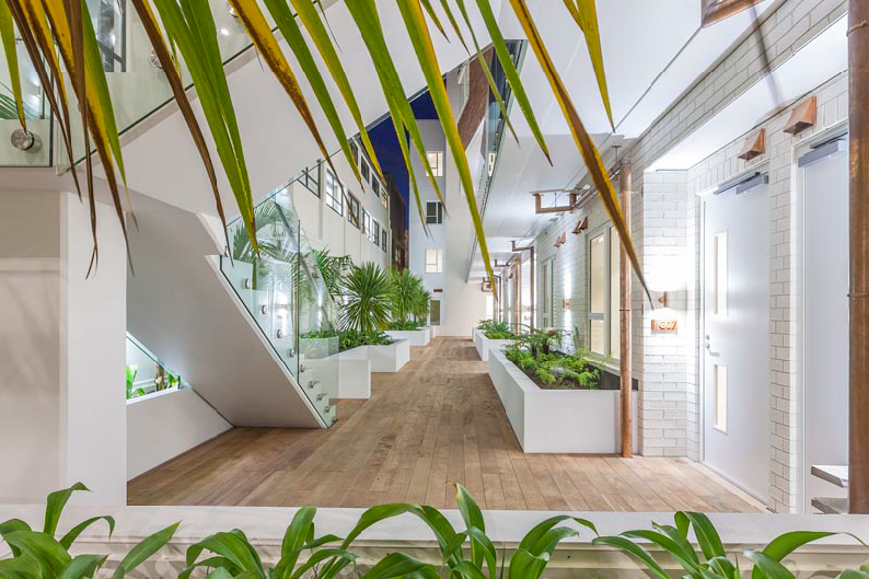 A luxurious, modern internal courtyard with plants, copper spouting, wooden floors and glass balconies.