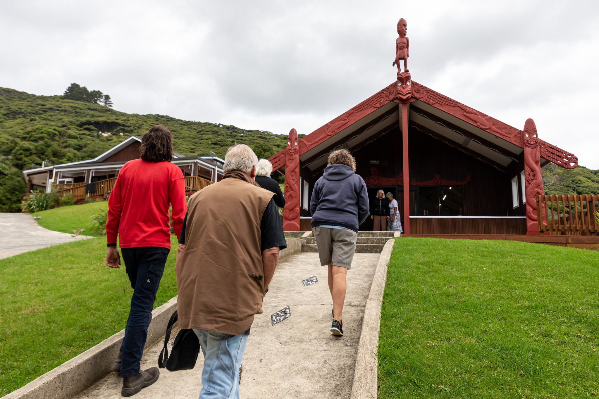 Four people approaching the wharenui of Kawa Marae, Aotea Great Barrier Island. 