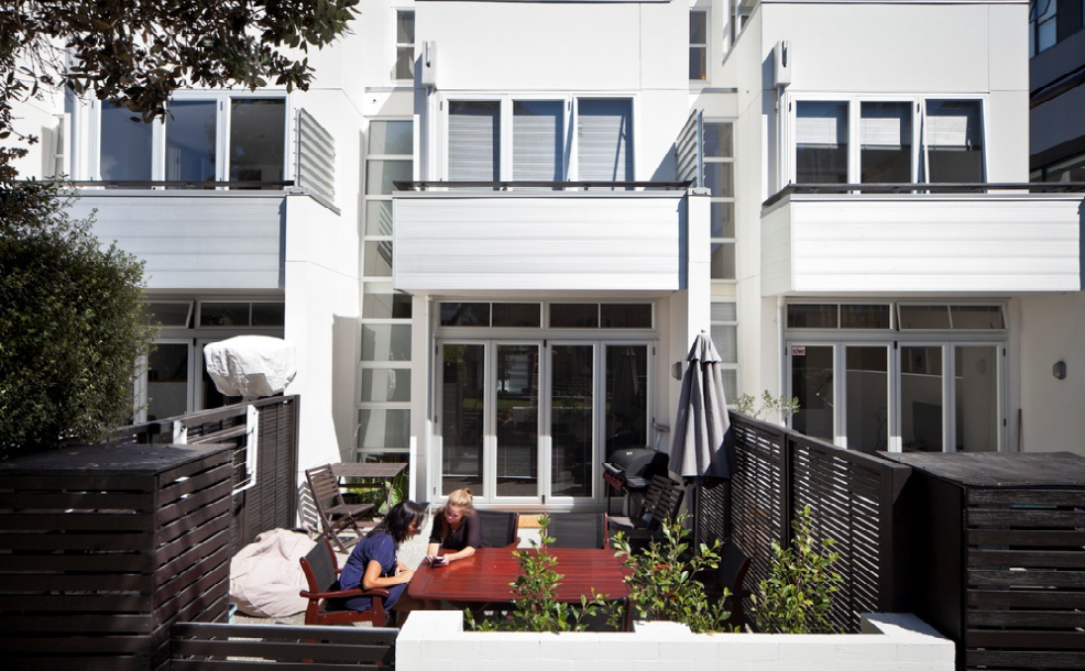 A cosy back yard with a garden table. Two people are sitting having a cup of tea under a tree.