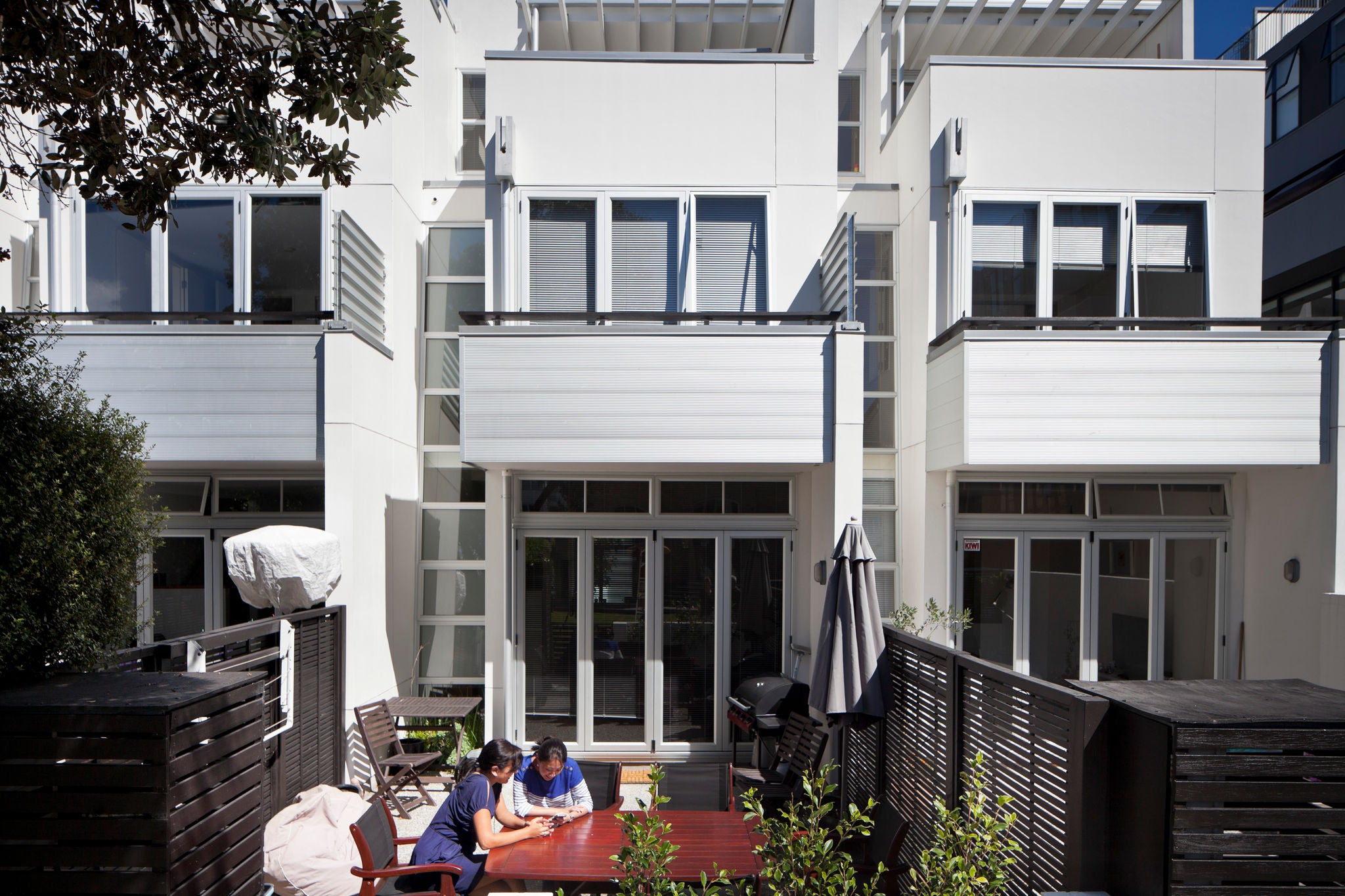 A cosy back yard with a garden table. Two people are sitting having a cup of tea under a tree.
