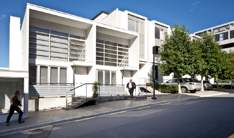 The terrace facade is bright in the sunny afternoon light, with bold modern lines offset by leady trees.