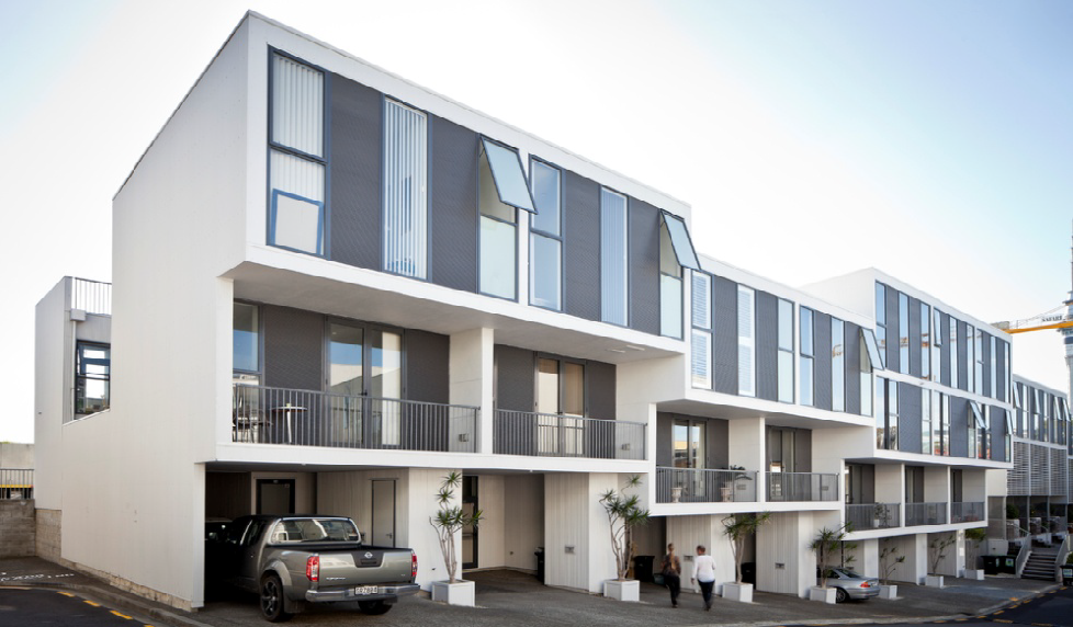 Looking from street-level at the apartments. They have bog windows and balconies with plants on ground level.