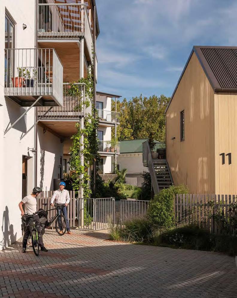 Two residents are about to set out on their bikes. The buildings behind them are covered with beautiful vines and plants.