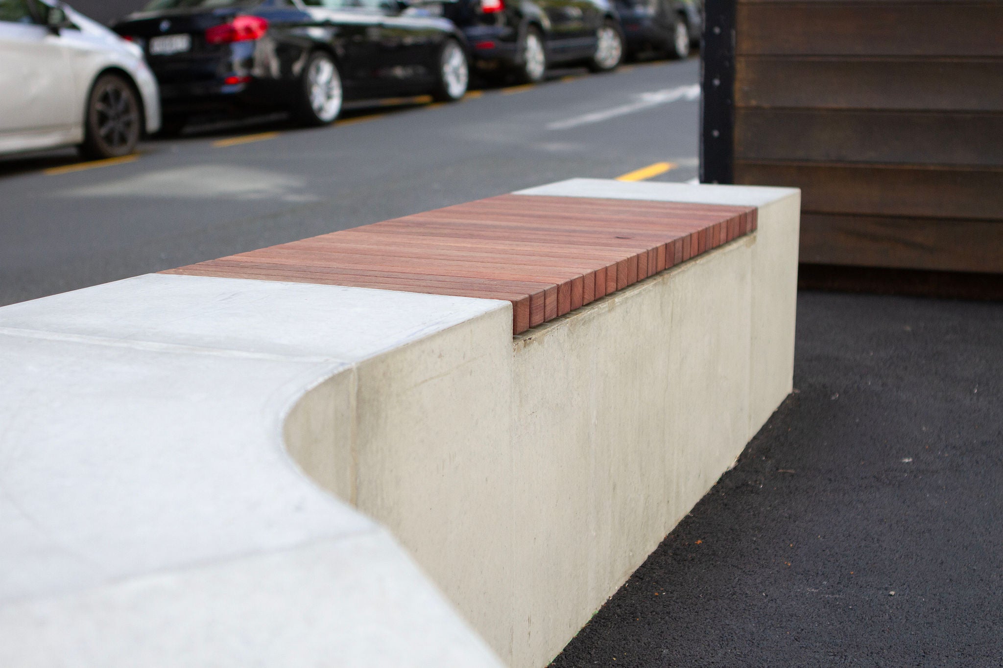 Looking close up at the wooden slats inset in a concrete bench at Paul street in downtown Auckland. The background is a blurry streetscape.