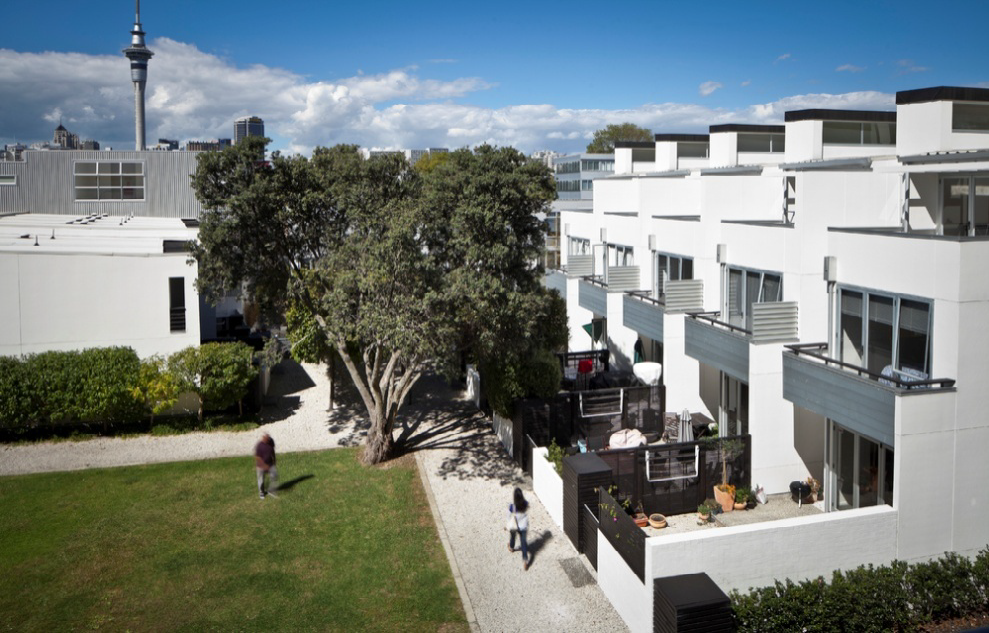 A wide green lawn hemmed with trees and terraces in the development.