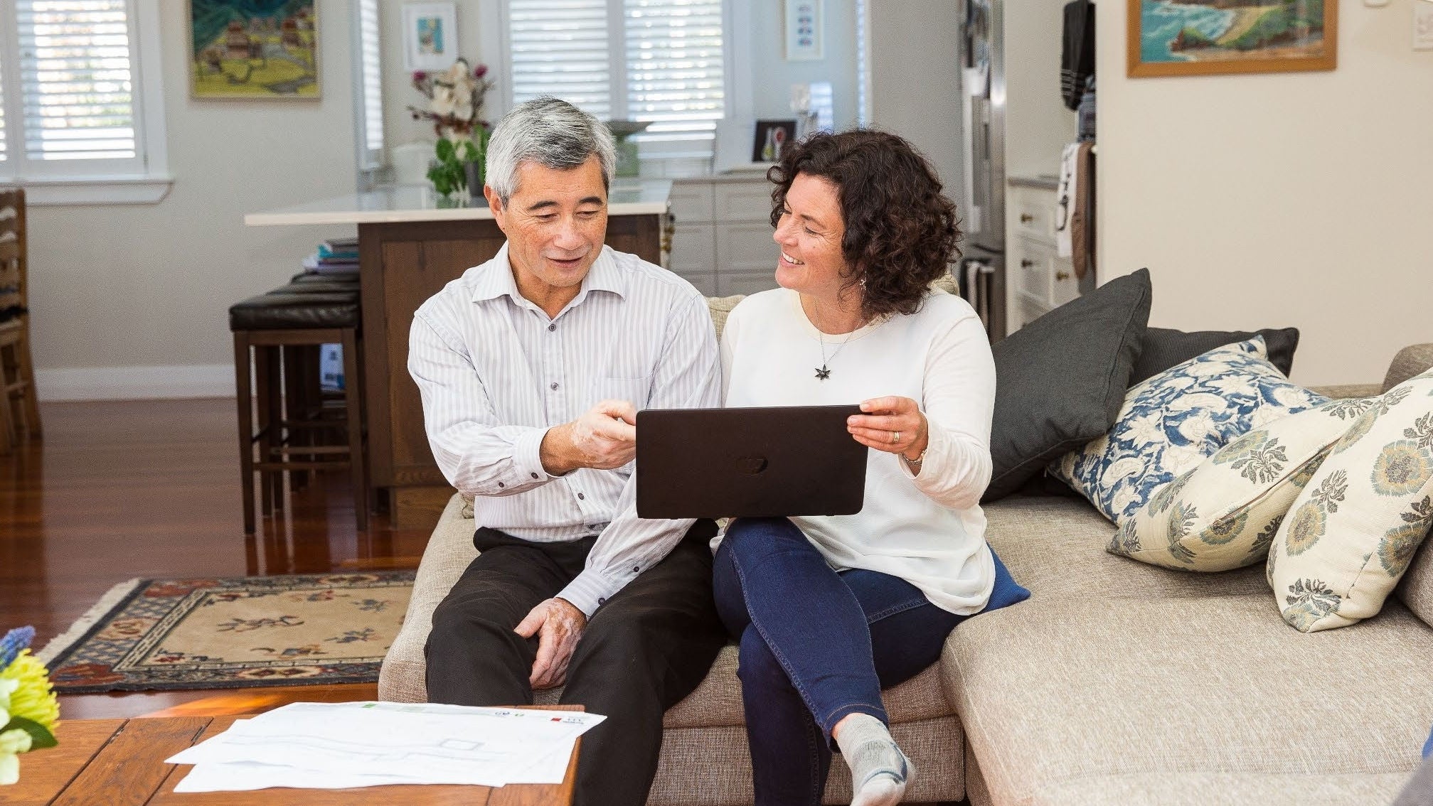 Design Statements A couple happily chatting on a sofa at home looking at something on an ipad or laptop.