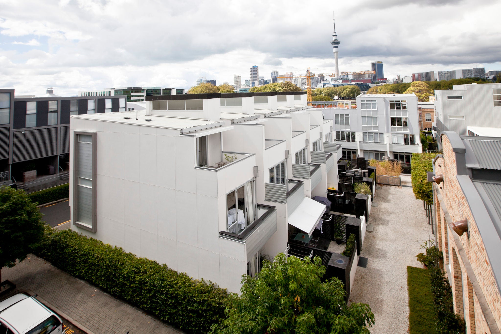  Beaumont Quarter - at the foot of an escarpment overlooking the Waitemata Harbour, the Beaumont Quarter sits across from Victoria Park on a site previously used for a gasworks. The site is in close proximity to central Auckland; we can see the city skyline, and the motorway passes nearby. There are trees buffering the homes from the noise of the city, the sky is blue and puffy clouds float by. 