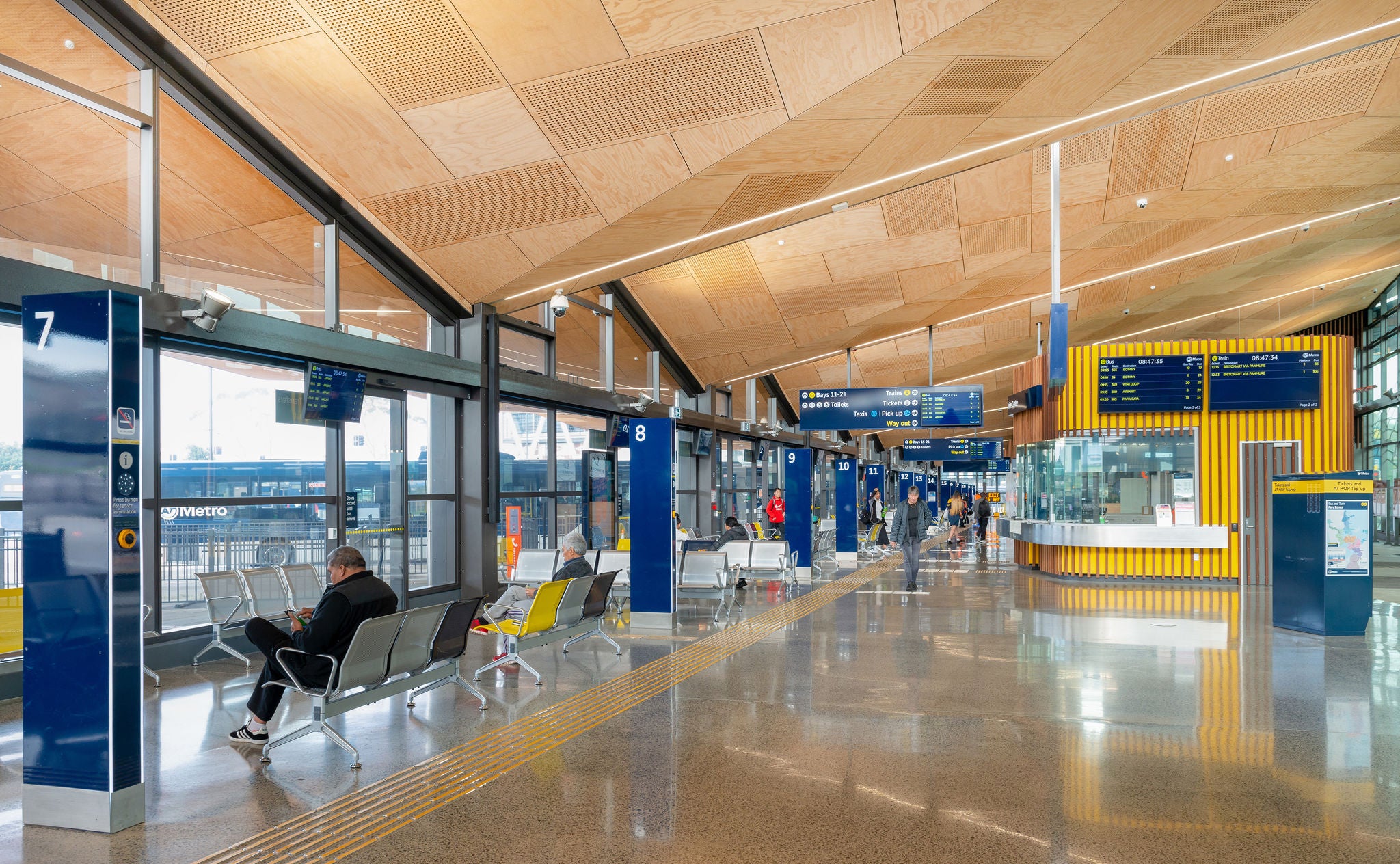 Station interior Inside the bust station looking up at the wood panelled ceiling, and blue and yellow Auckland transport livery on the bus gates.
