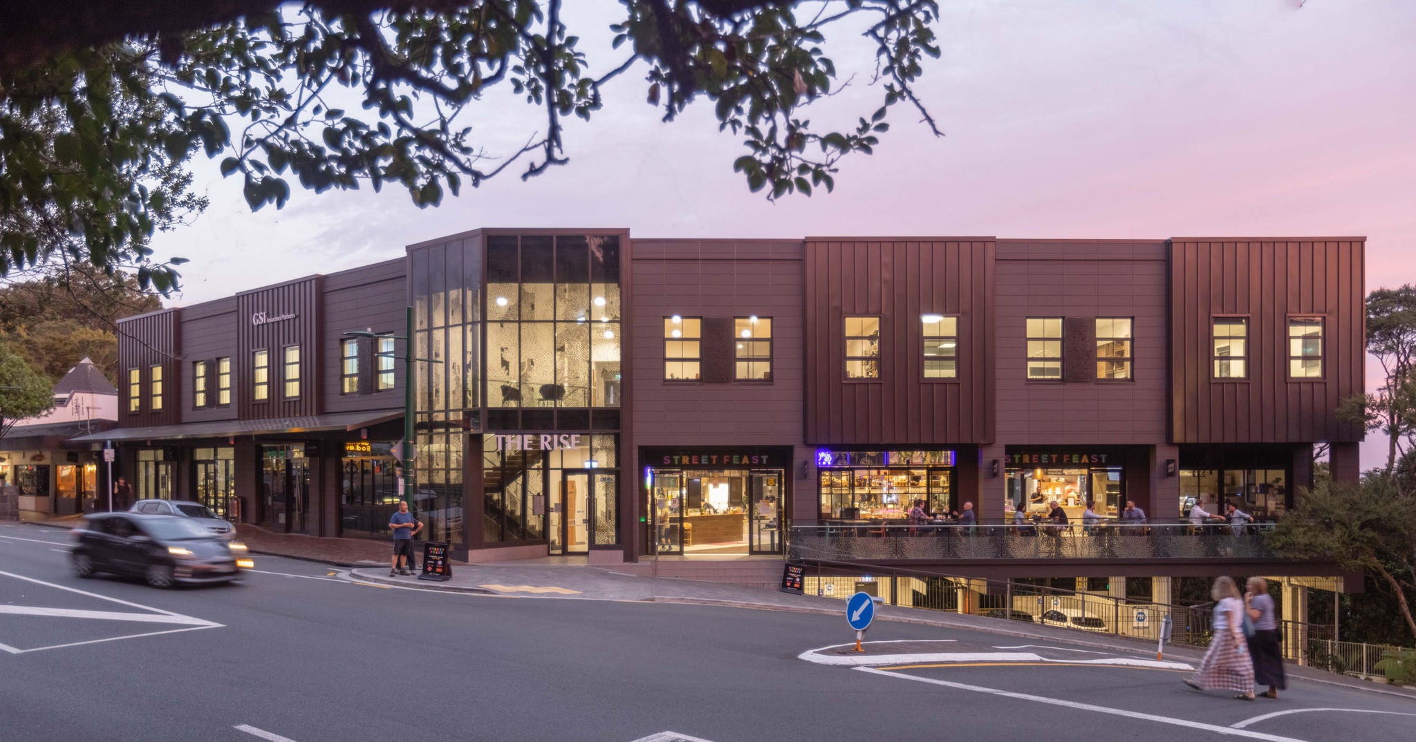 Corner elevation photo of The Rise at dusk with cars and people crossing the road.