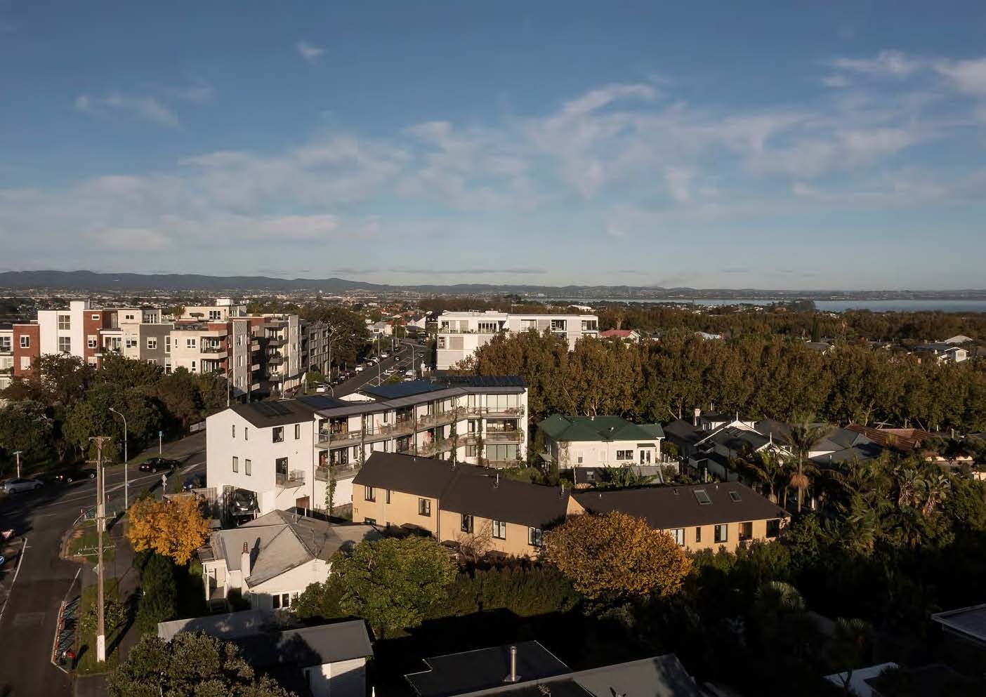 A bird's-eye view of the development; there are apartment blocks over the road in the background, with the Waitemata harbour and Waitakere mountains in the distance.