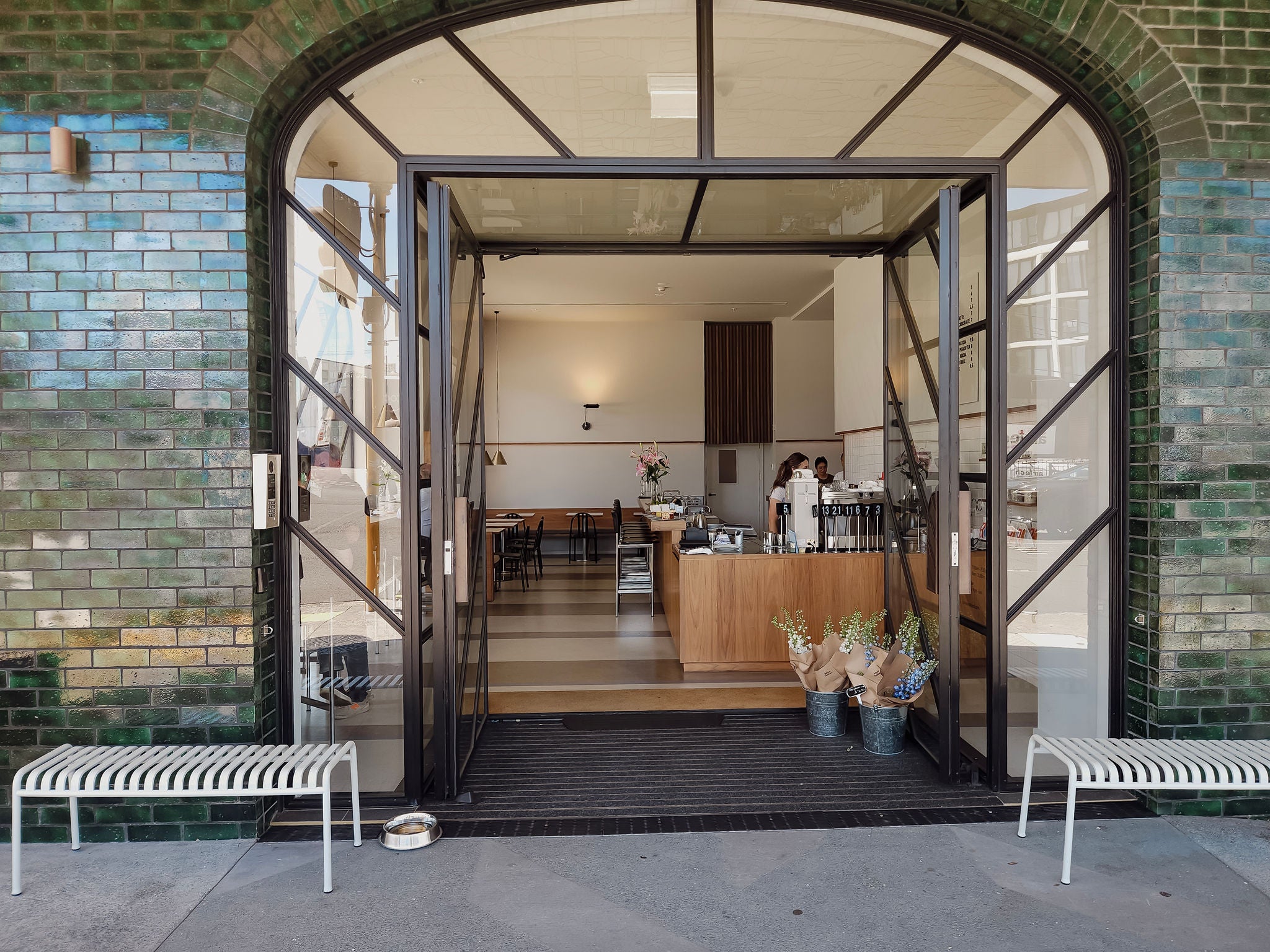 Looking inside the cafe called Juno, with white benches outside the front door and flowers for sale inside the internal entry.