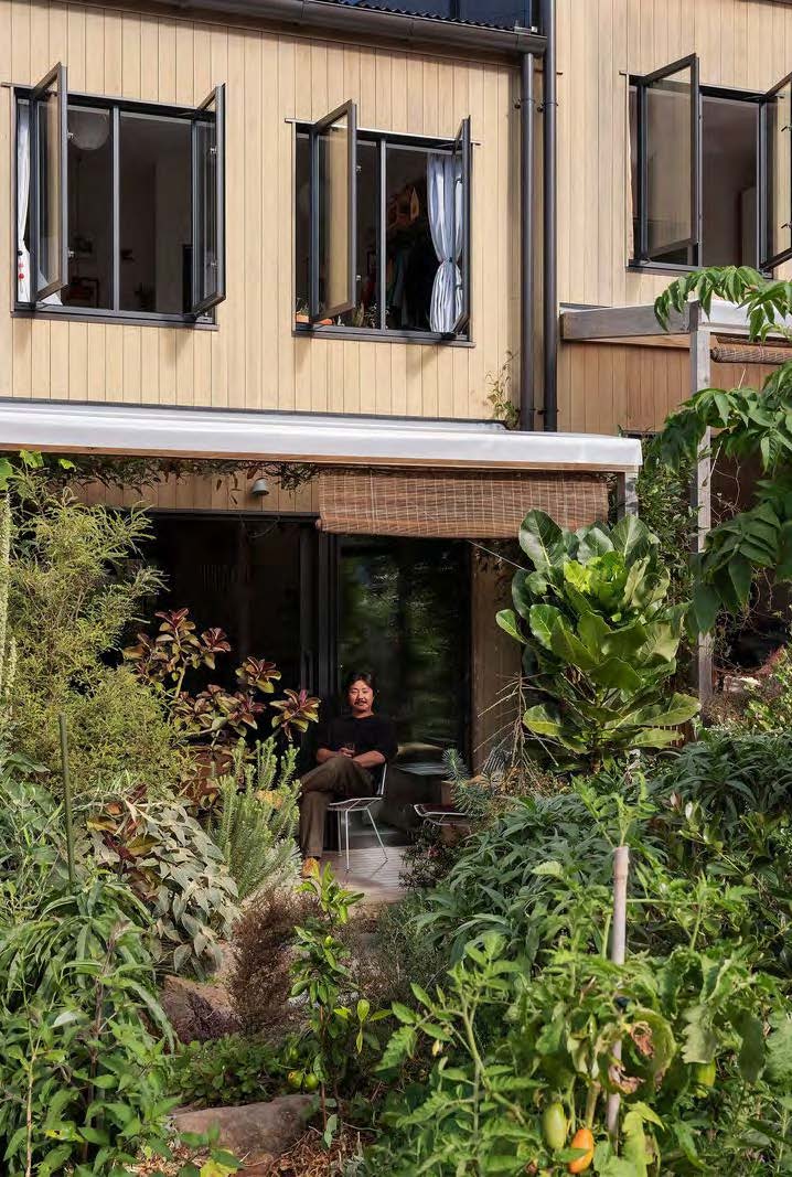 A resident sits on the ground floor porch looking very happy at the plants growing outside his home.