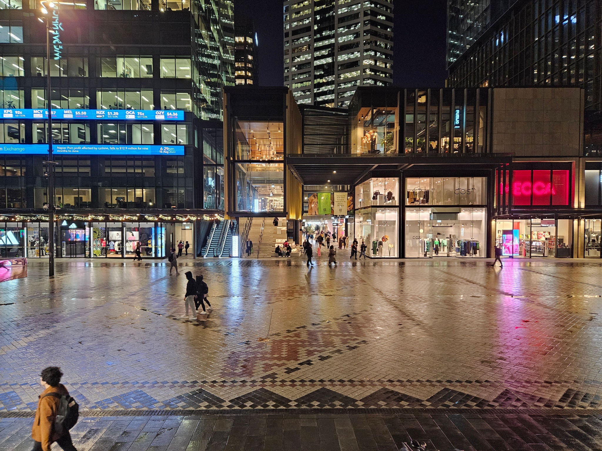 Te Komititanga (Britomart) at night, with people walking in the square after a bit of rain