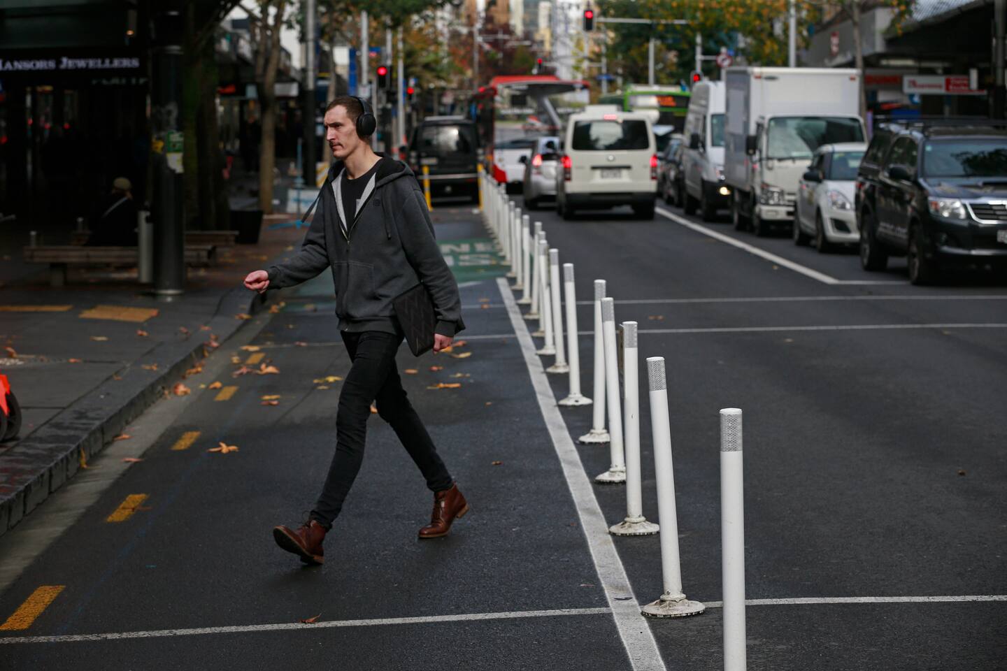A person walking on Queen Street with hit sticks marking the edge of the extended footpath.