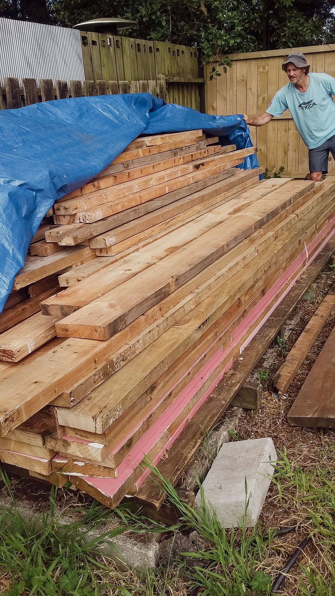 Blair lifting a tarp off the pile of timber planks recovered from the old building.