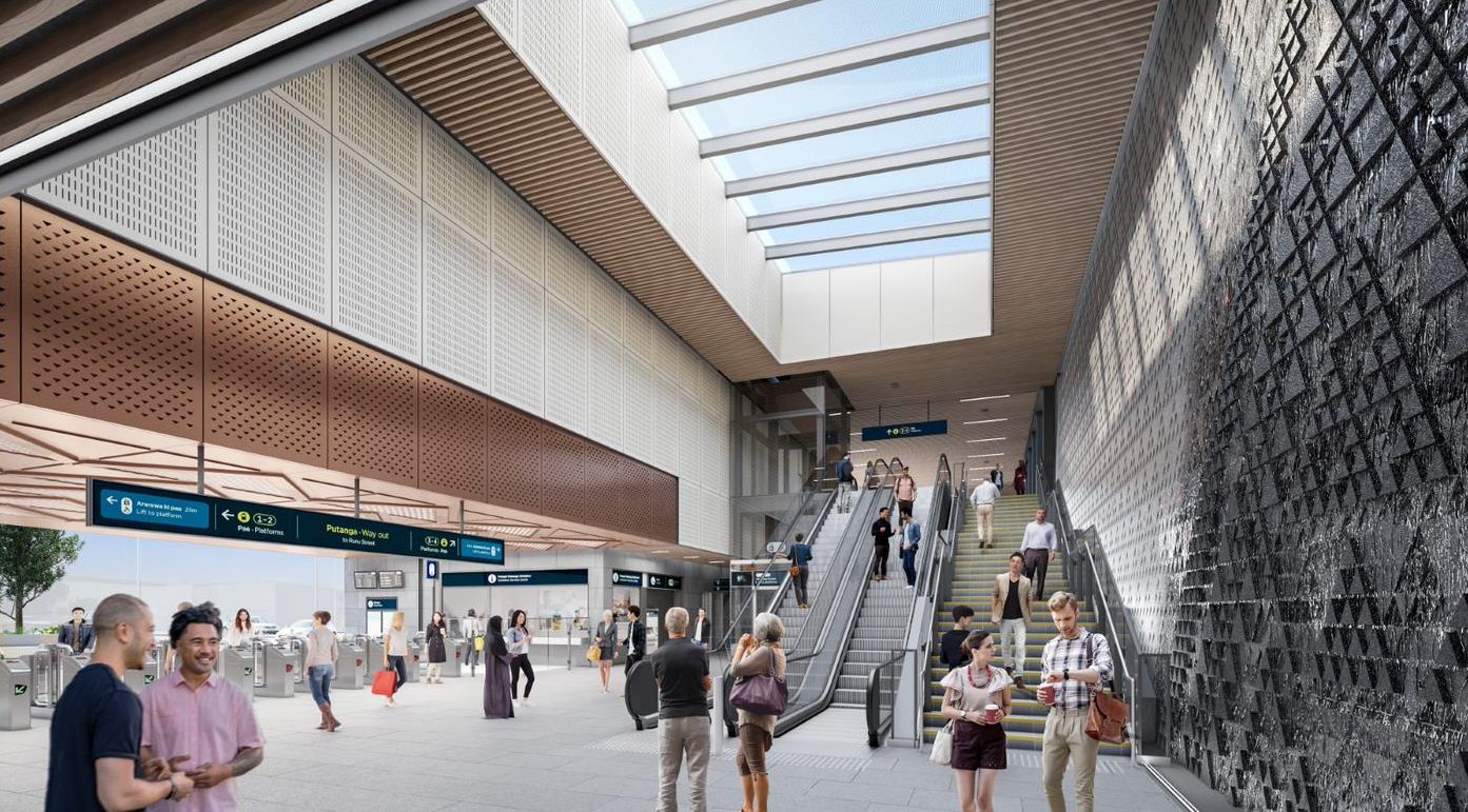 A render of the interior of Maungawhau station. There are people walking around inside through the turnstiles, up and down the escalators and past the beautiful basalt wall made from rock found in Mt Eden.