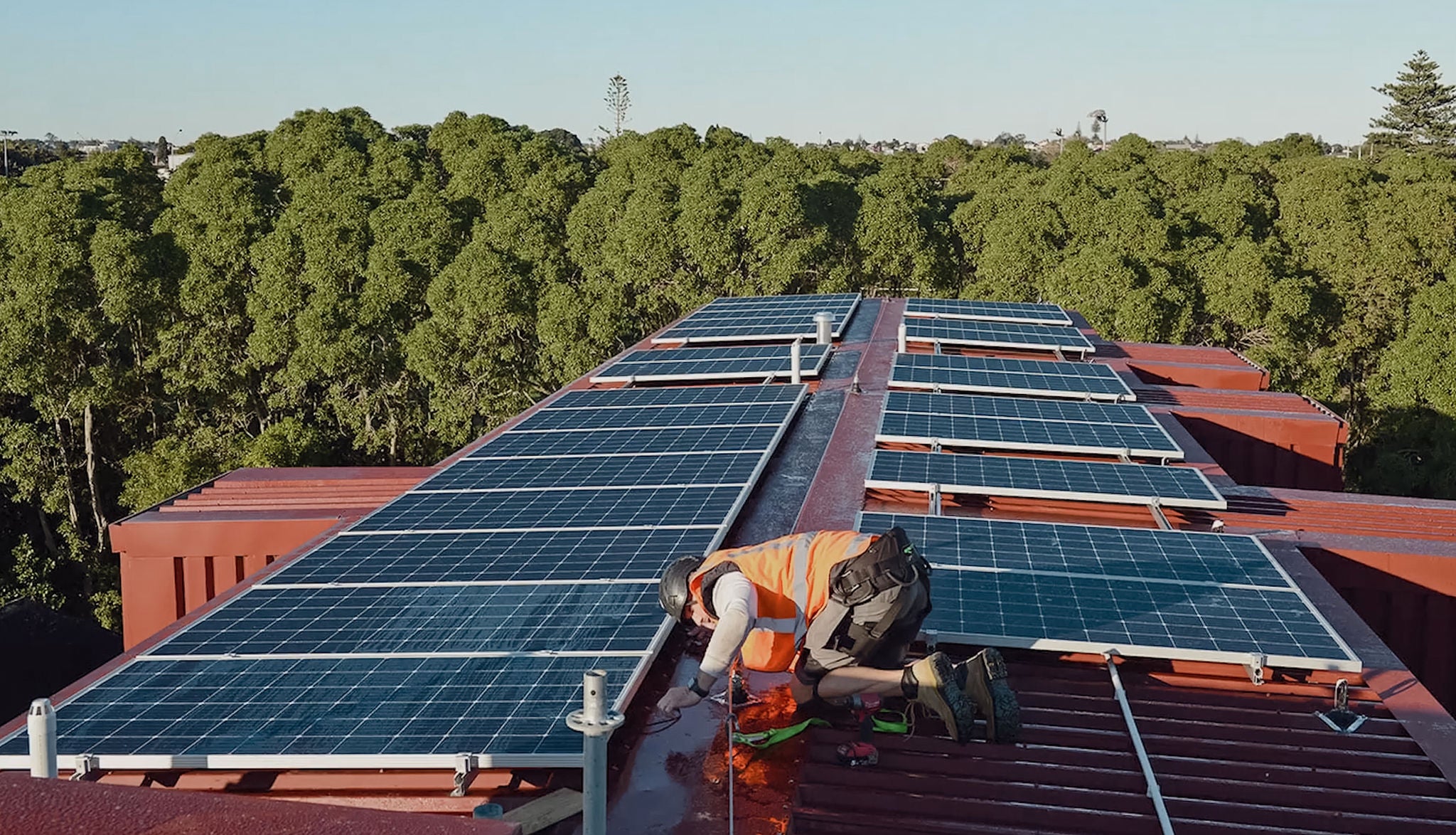 A tradie works to install solar panels on the roof of the apartments. 