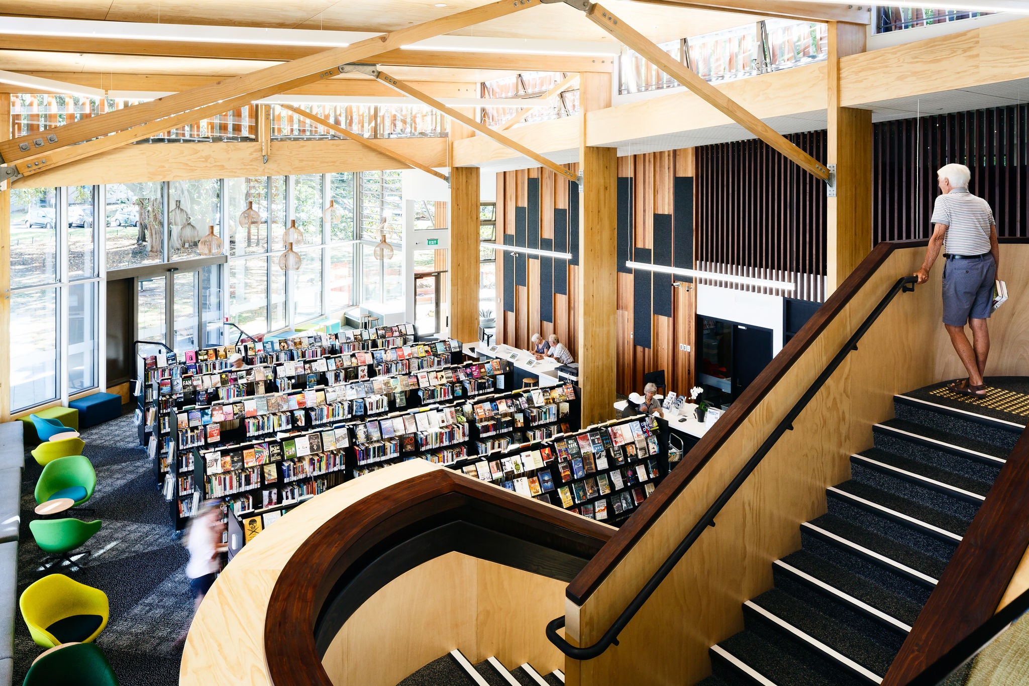 An elderly man is standing at the top of the stairs holding the bannister looking out over the atrium and the myriad of books available.