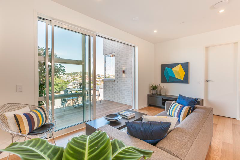 A modern apartment interior, looking out at the recessed balcony. It has a great view of one of Auckland's maunga.