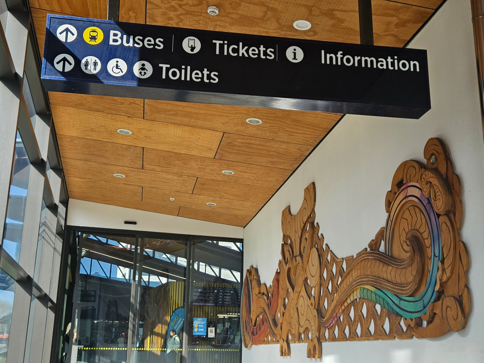 Colourful māori carving in a public space in the station Looking at a māori cwood arving mounted on a wall in a public space in the station. Colours are woven into the wings of the carving.