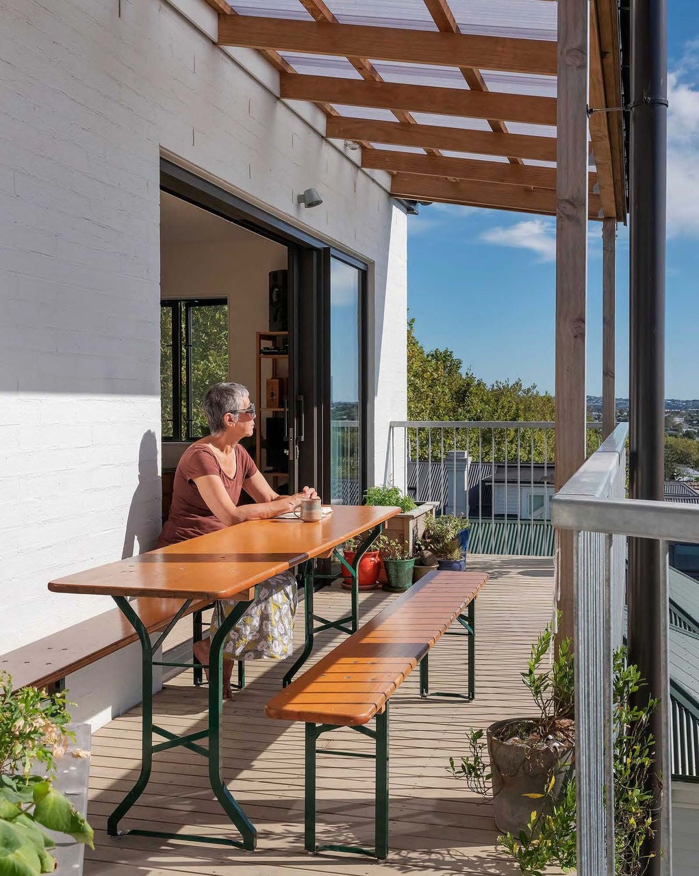 A lady sits on her balcony looking at the view while having a cup of tea.