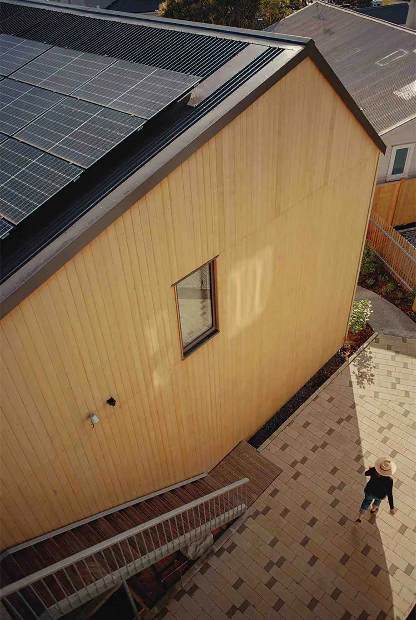 Looking down at the blonde teak Abodo Vulcan cladding. A person is walking past on the decorative paving stones below.