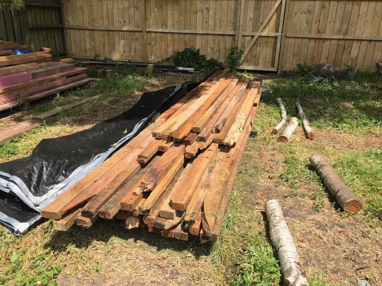 A pile of rimu beams laid on the grass outside the bungalow.