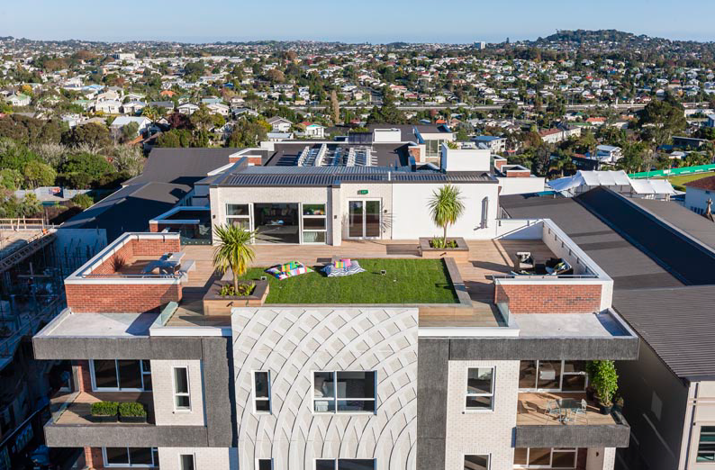 A bird's eye view of the apartment block; there is a patch of lawn with cushions and plants where people can sit and relax.