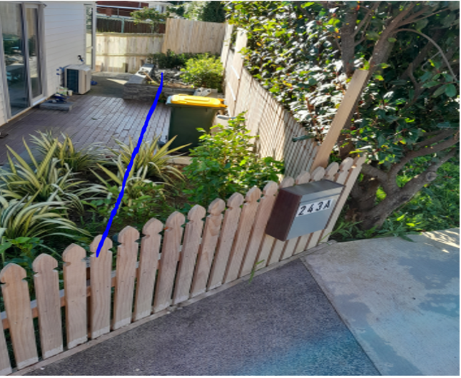 A small backyard surrounded by a picket fence, a blue line indicates where the pipe runs under the yard.