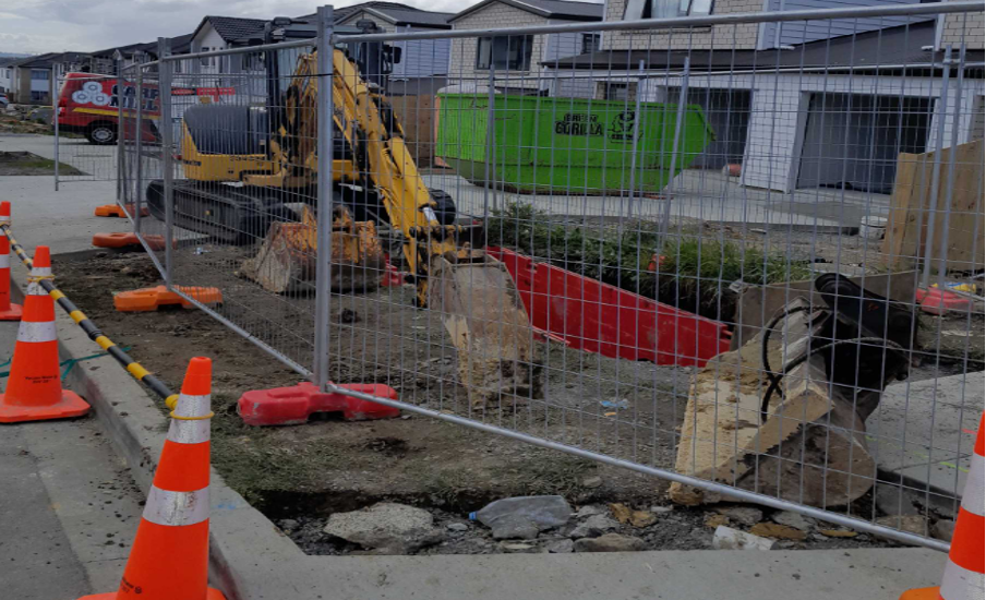 A digger ripping up the sidewalk to expose the blocked pipe.
