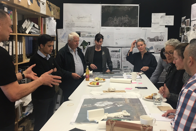 Mana Whenua kaitiaki (guardians) and designers are grouped around a table with plans and models engaged in the co-design process at Isthmus’ studio.  