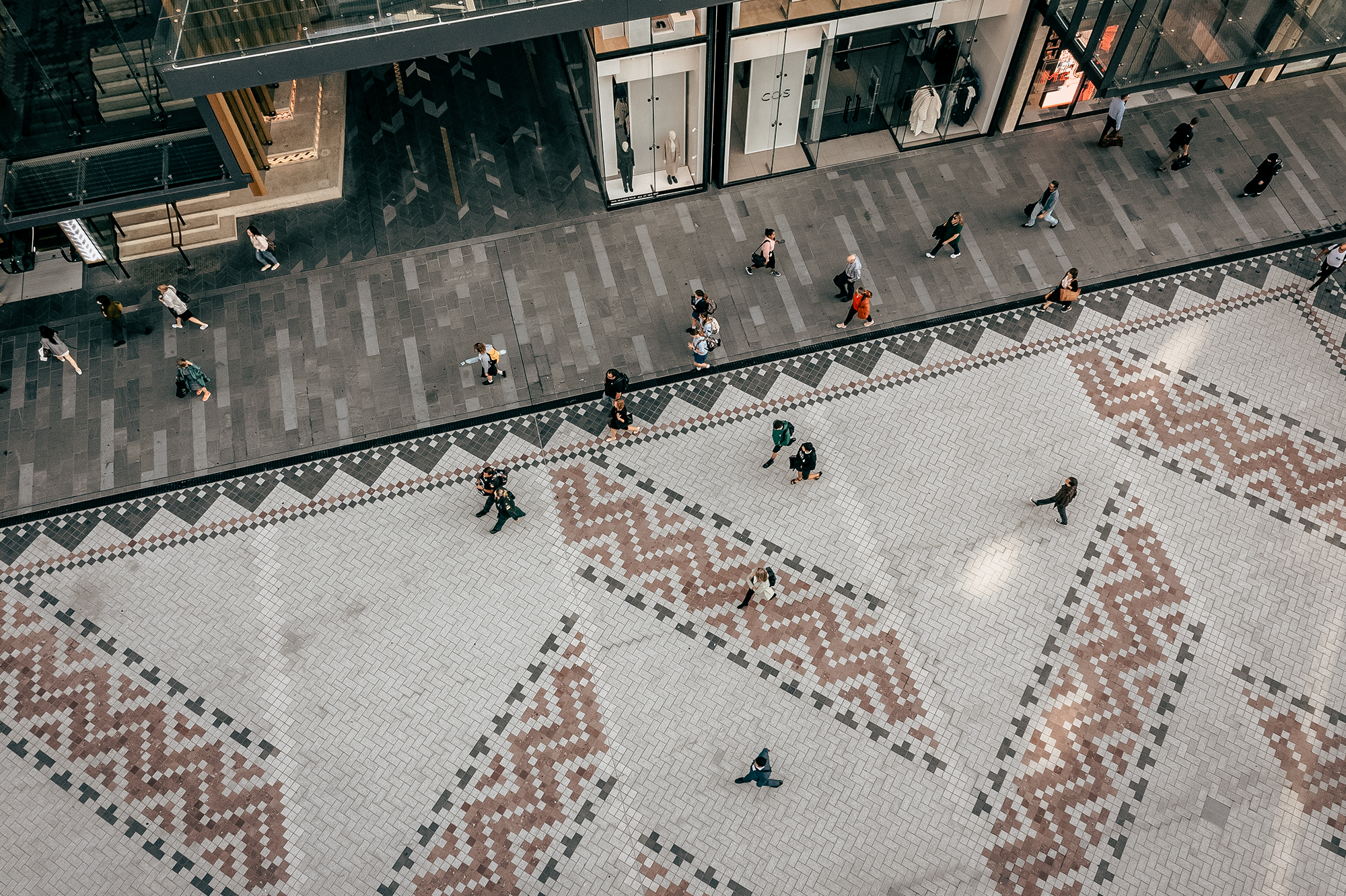Aerial view of the public space located adjacent to Commercial Bay and Waitematā Station at Lower Queen Street, with basalt pavers that form a whāriki (welcome mat) designed by Mana Whenua weavers to depict a woven harakeke (flax) mat. 